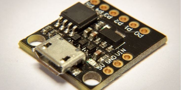 Nahaufnahme einer kleinen schwarzen Mikrocontroller-Breakout-Platine mit einem Micro-USB-Anschluss, oberflächenmontierten Bauteilen und beschrifteten Pinlöchern auf weißem Hintergrund.