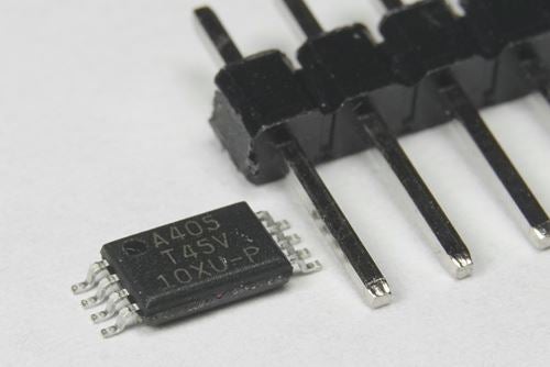 Close-up of a small surface‑mount integrated circuit labeled “A405 TKSV” placed beside a black pin header on a white background.