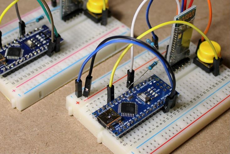 Un primo piano delle schede Arduino montate su breadboard, collegate a moduli Bluetooth con cavi jumper, resistori e pulsanti gialli.