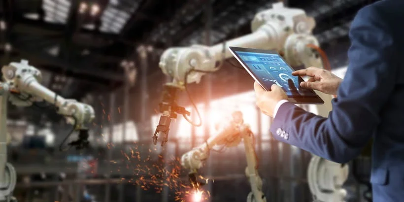 A person in business attire operates a digital tablet in a modern factory setting.