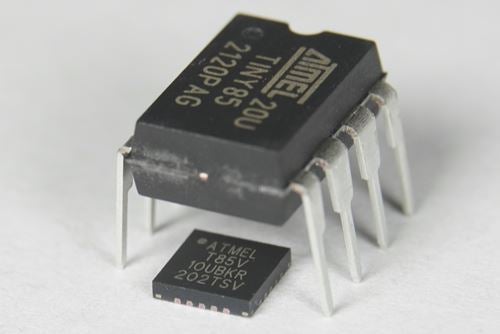 Comparison of two Atmel microcontroller chips, one larger DIP package standing on metal pins and one smaller surface‑mount package, shown on a white background.