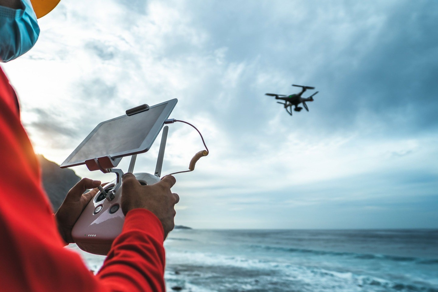 A person operates a drone using a handheld remote control with a screen, overlooking a vast ocean