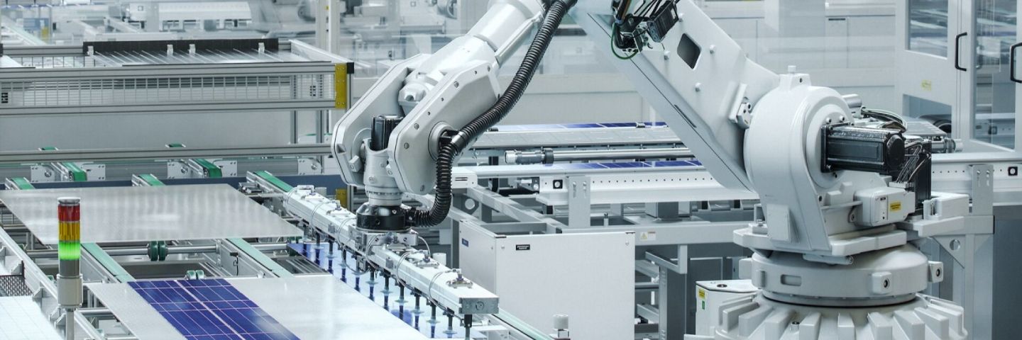 Un brazo robótico industrial blanco está ensamblando activamente paneles solares en una línea de producción en un entorno moderno y automatizado de fábrica.