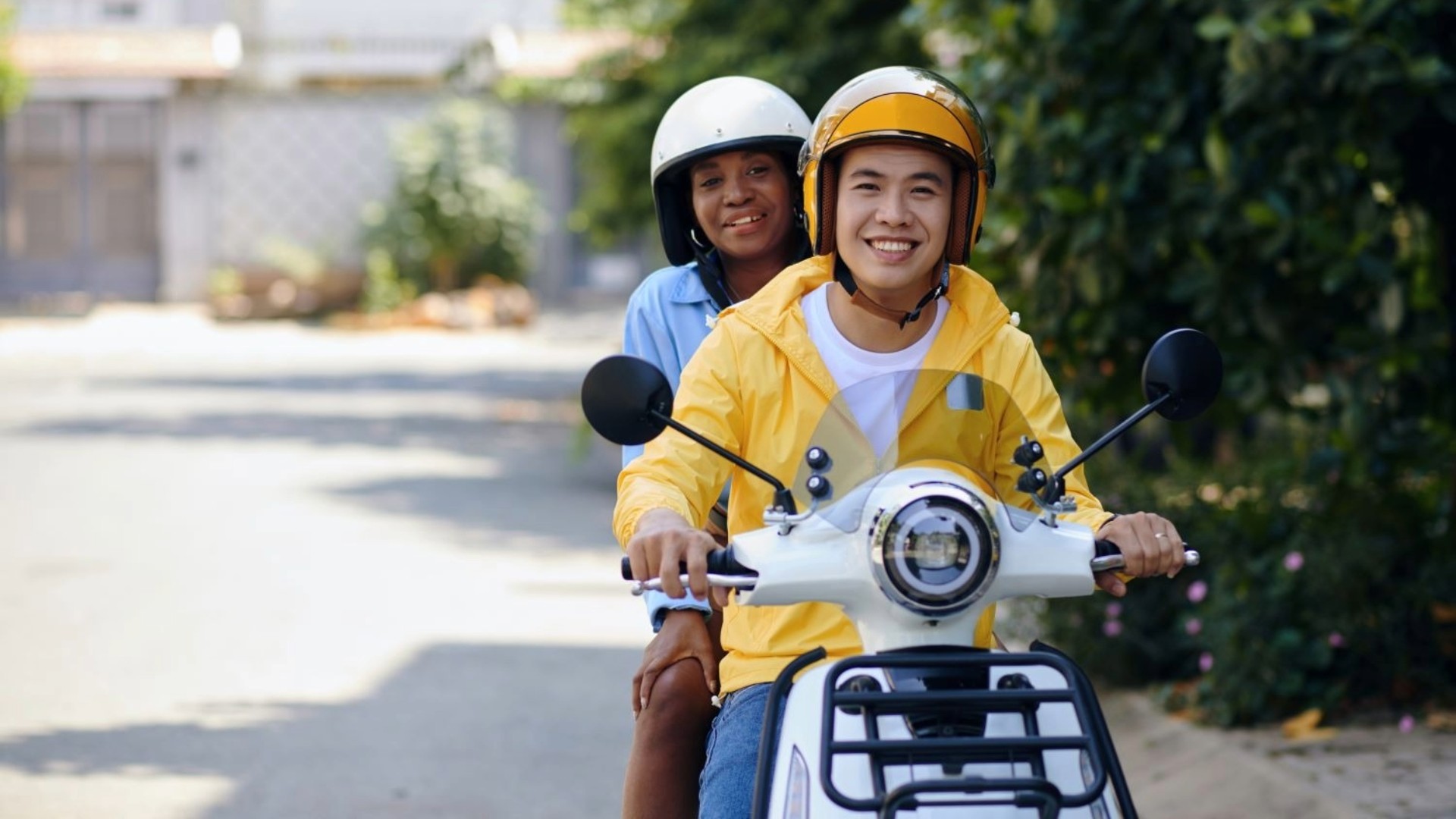 A pair of individuals ride a white scooter on a sunny day.