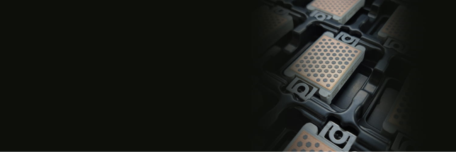 Wide banner image showing a close‑up of silicon carbide power modules with perforated metal contact pads housed in dark rectangular frames, arranged in a grid pattern with shallow depth of field and a dark gradient on the left, illustrating advanced power electronics packaging.