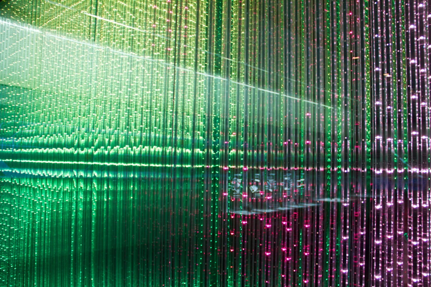 An abstract installation composed of vertical lines illuminated by green and pink lights.