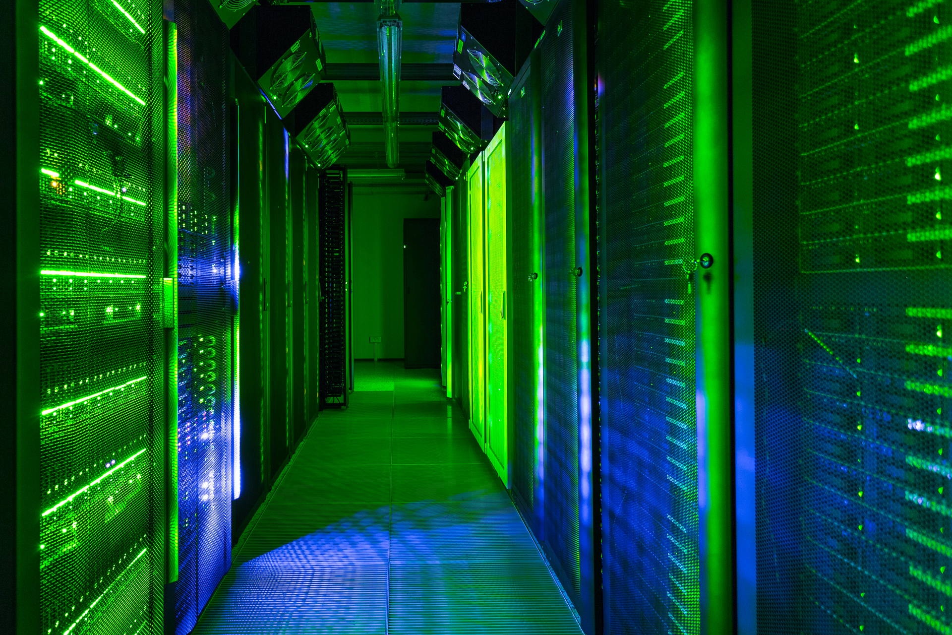 Un pasillo bien iluminado en un moderno centro de datos cuenta con filas de racks de servidores que brillan con luces LED verdes y azules.
