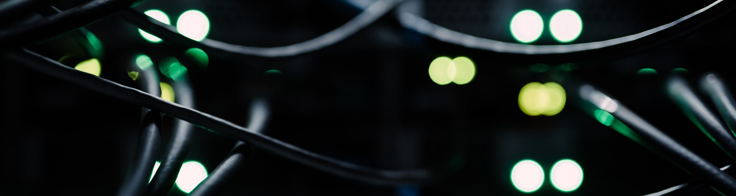 Esta imagen muestra una vista de cerca de cables de red conectados a un rack de servidores, con múltiples luces indicadoras verdes y amarillas brillando en el fondo.
