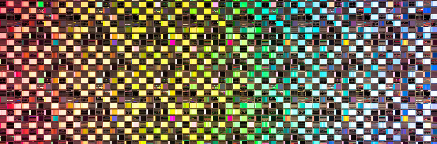 A close-up view of a microchip grid featuring a vibrant gradient of colors transitioning from warm yellows to cool blues.